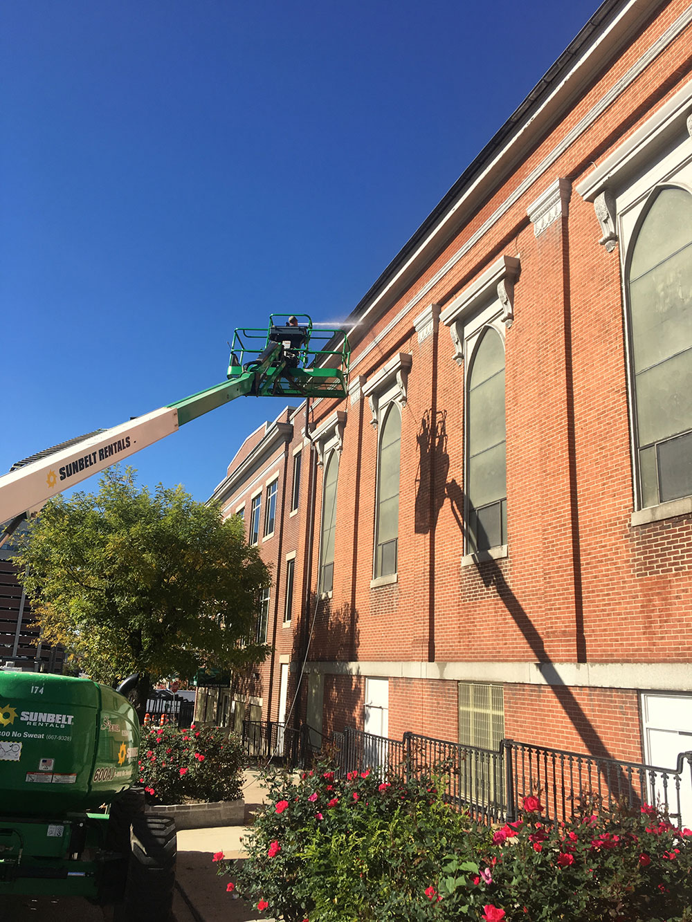 Technician using a boom lift to pressure wash the upper brick exterior of a church building, removing dirt and restoring a clean appearance.