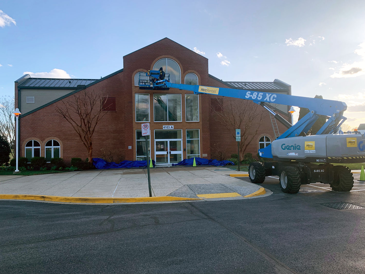 Technicians using a boom lift to pressure wash the exterior windows and brick facade of a commercial building for a clean, professional appearance.