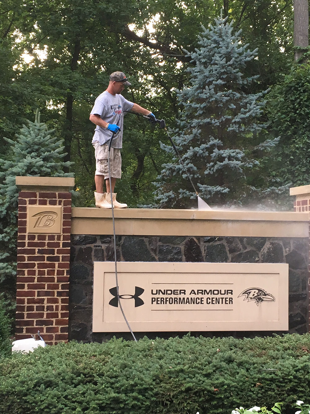 Technician pressure washing a commercial entrance sign to remove dirt, stains, and buildup, restoring a clean and professional appearance.