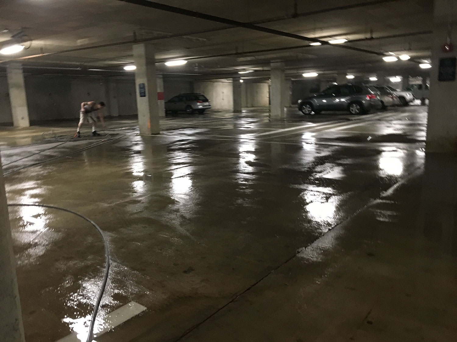 Professional pressure washing a concrete parking garage floor to remove dirt, oil stains, and grime, improving cleanliness and safety.